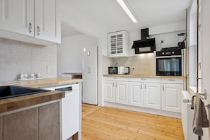 A modern kitchen with white cabinets, a wooden countertop, a built-in oven, and a microwave.