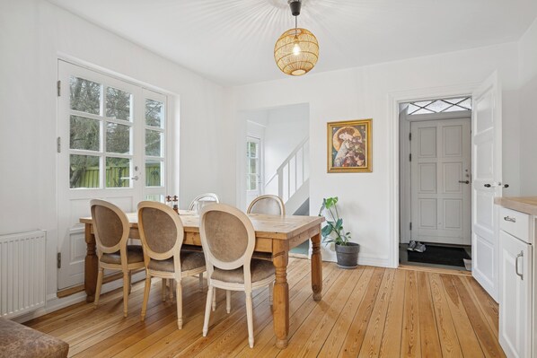 A dining area with a wooden table and chairs, a hanging light fixture, and a staircase leading to another room.