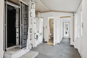 A hallway with a shower, a washing machine, and a staircase leading to another room.