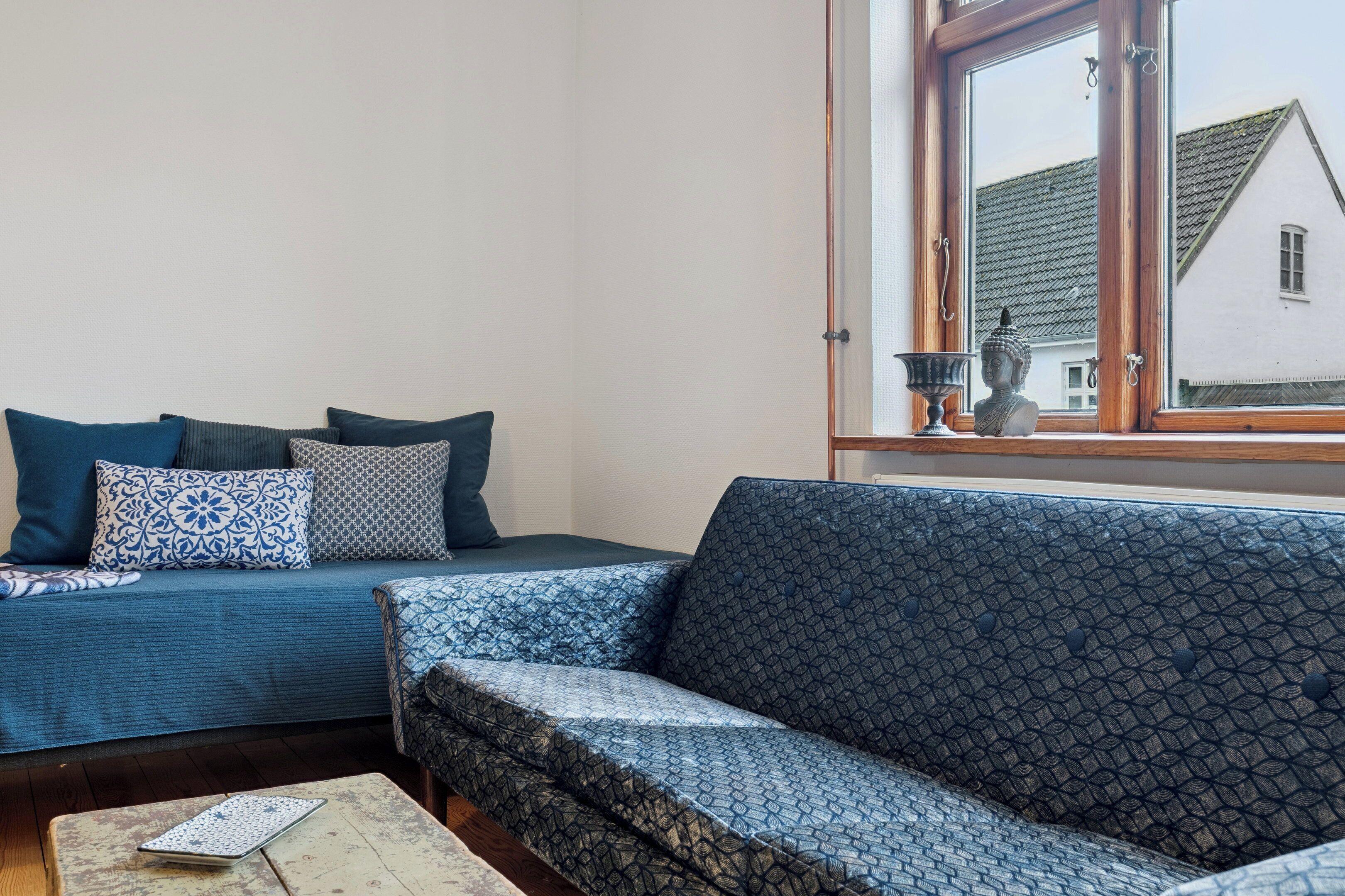 A living room with a blue patterned sofa, a patterned armchair, and a small table with a remote control.