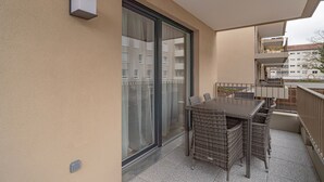 Ein Balkon mit Tisch und Stühlen, eine Schiebetür und Blick auf andere Gebäude.