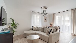 Ein modernes Wohnzimmer mit einem Ecksofa, einem Glastisch, einem Flachbildfernseher und einer dekorativen Pendelleuchte.
