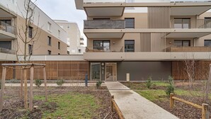 Ein modernes Mehrfamilienhaus mit einem Innenhof, Holzzäunen und einem Betonweg.
