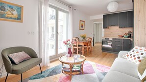 Een moderne woonkamer met een bank, fauteuil en een eettafel met stoelen. Er is een keuken met kasten en een fornuis.
