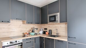 Een moderne keuken met grijze kastjes, een houten aanrecht, een inbouwoven, een magnetron en een spoelbak.