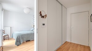 Een slaapkamer met een bed, een stoel, een radiator, een wandthermostaat en een deur.