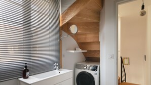 Een kleine wasruimte met een wasmachine, een wasbak en een raam met zonwering.