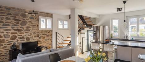 Un espacio moderno para vivir con una pared de piedra, un sofá gris, una mesa de comedor con individuales y una zona de cocina con electrodomésticos de acero inoxidable.
