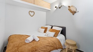 A bedroom with a bed, a wooden headboard, a heart-shaped decoration, a turtle wall art, and a woven stool. - Cocon Bel Azur - 300m de la Plage (Roquebrune-sur-Argens)