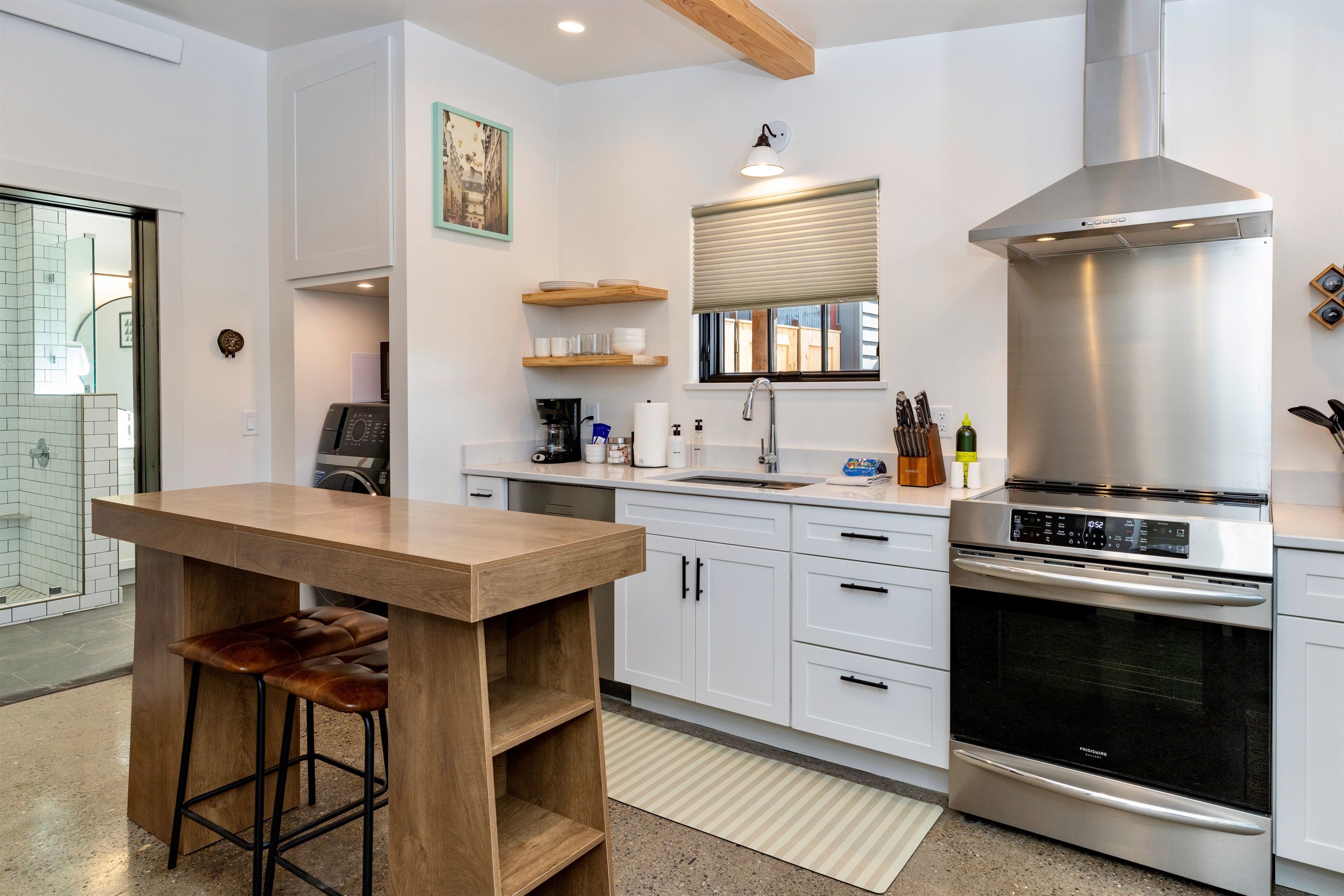 A modern kitchen with white cabinets, a stainless steel range hood, and a wooden bar stool.