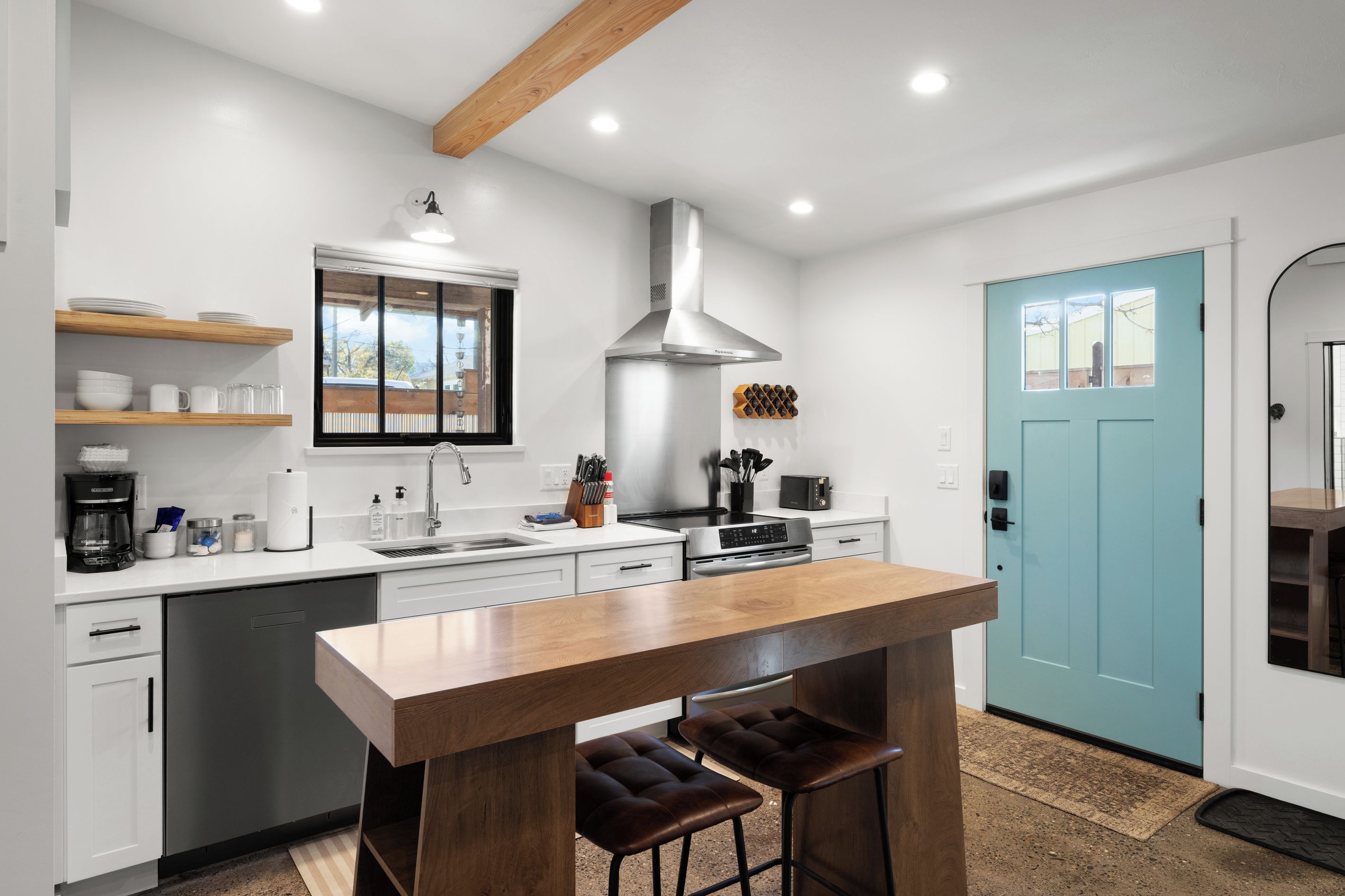 A modern kitchen with a central island, bar stools, and a blue door.