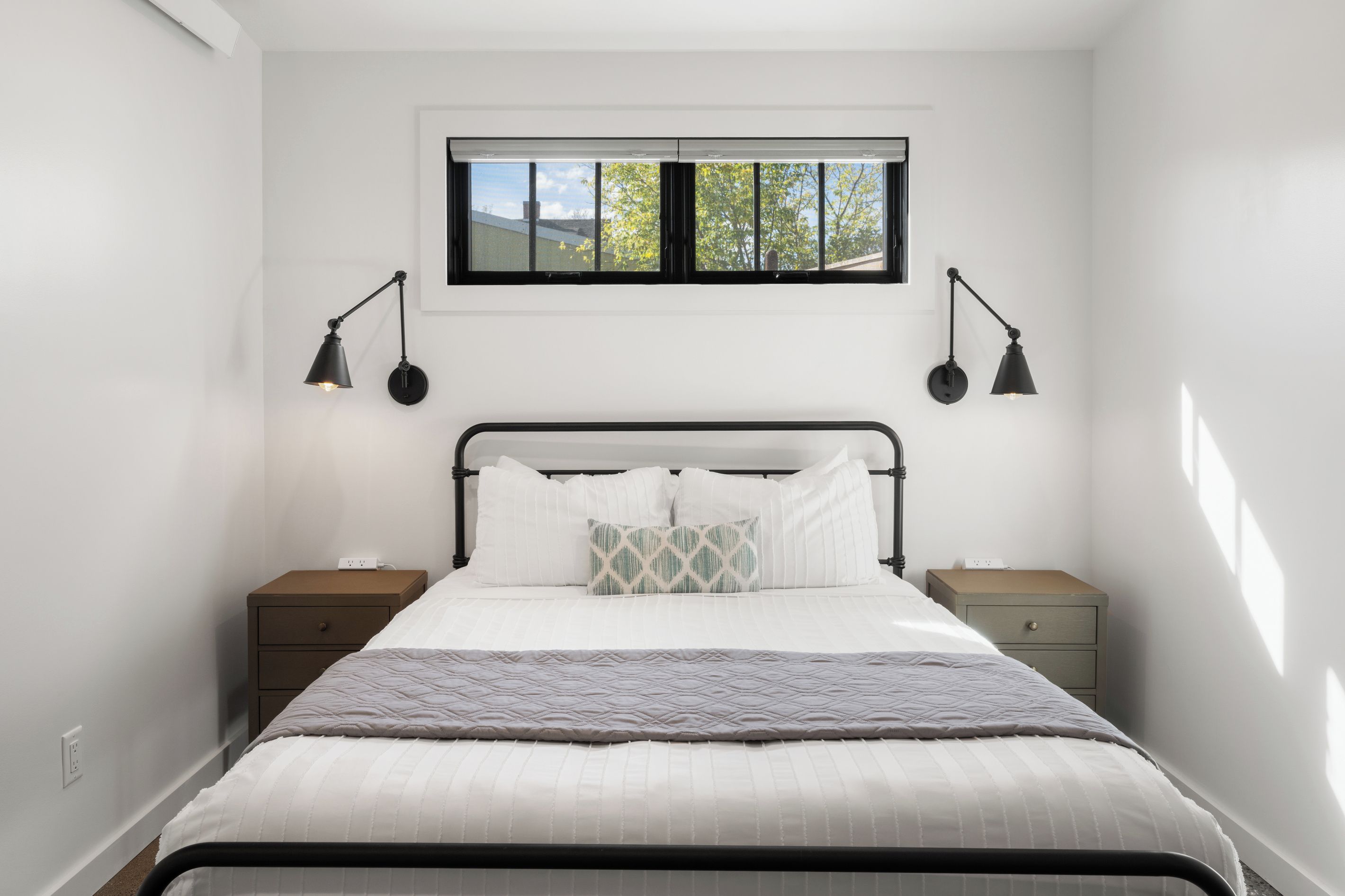 A bedroom with a bed, two bedside tables, a window, and two wall-mounted lamps.