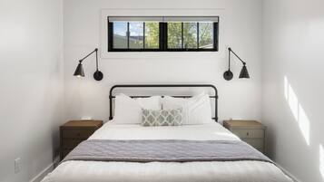 A bedroom with a bed, two bedside tables, a window, and two wall-mounted lamps.