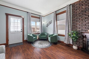 A room with hardwood flooring, a white door, two green armchairs, a patterned rug, and a brick wall. - Dog Friendly Historic Home (Anaconda)