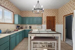 A kitchen with teal cabinets, a white countertop, a dining table with a bench, a chandelier, and a microwave.