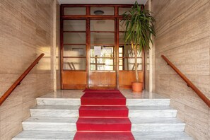 Una scalinata in marmo con un tappeto rosso che conduce a una porta in legno con pannelli di vetro.