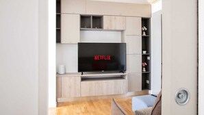 Una sala moderna con un televisor de pantalla plana montado en un mueble de madera, una mesita blanca y un sofá.