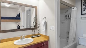 A bathroom with a wooden vanity, a large mirror, a white sink, and a shower area.