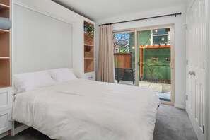 A bedroom with a large bed, built-in shelving, a sliding glass door to a patio, and a view of the outdoors. - Bright West Seattle 3BR • EV Parking • Walkable • Near Stadiums (Seattle)