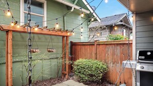 A backyard with a wooden deck, a swing, a barbecue grill, and string lights.