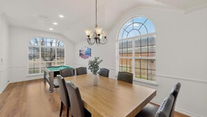 Une pièce spacieuse avec une grande table en bois, plusieurs chaises, un billard et un lustre.