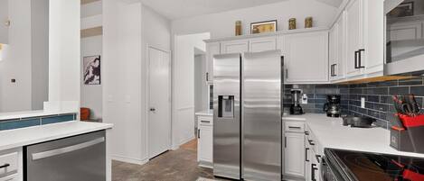 A modern kitchen with white cabinetry, stainless steel appliances, and a blue patterned rug.