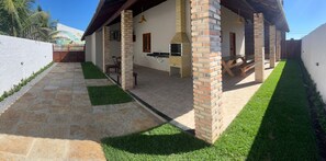 A covered outdoor patio with a brick chimney, stone flooring, and a small lawn area. - Casa Al Mare - Barro Preto Beach (Luís Correia)