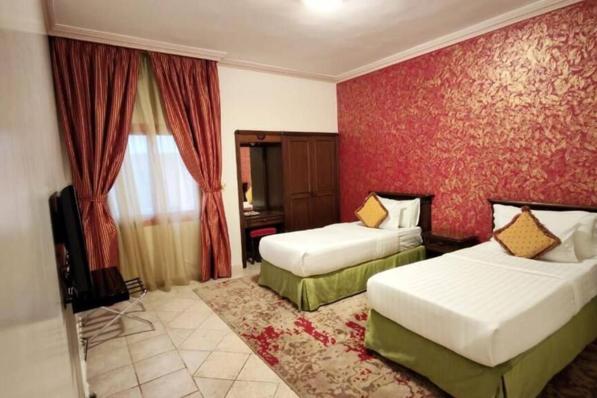 A hotel room with two single beds, a wardrobe, a mirror, and a television.