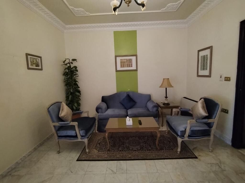 A living room with a sofa, two armchairs, a coffee table, a lamp, and a plant.