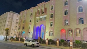 A multi-story hotel with a pink facade, illuminated windows, and a white car parked in front. - Rotana Furnished Apartments (Jeddah)