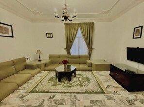 A living room with a sofa set, a coffee table, a TV, and a chandelier. - Rotana Furnished Apartments (Jeddah)