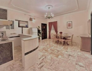 A compact kitchen with a sink, stove, and cabinets, a dining area with a table and chairs, and a chandelier. - Rotana Furnished Apartments (Jeddah)