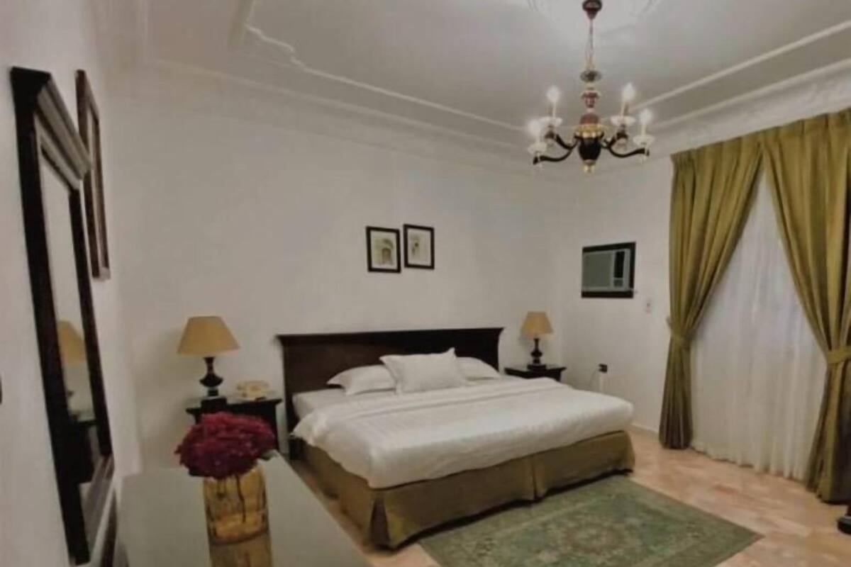 A hotel room with a large bed, a desk, a chandelier, and a green rug.