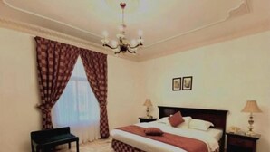 A bedroom with a large bed, a bench, a chandelier, and a rug. - Rotana Furnished Apartments (Jeddah)