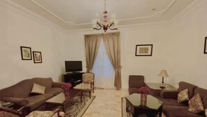 A living room with two sofas, a coffee table, a TV, and a chandelier. - Rotana Furnished Apartments (Jeddah)