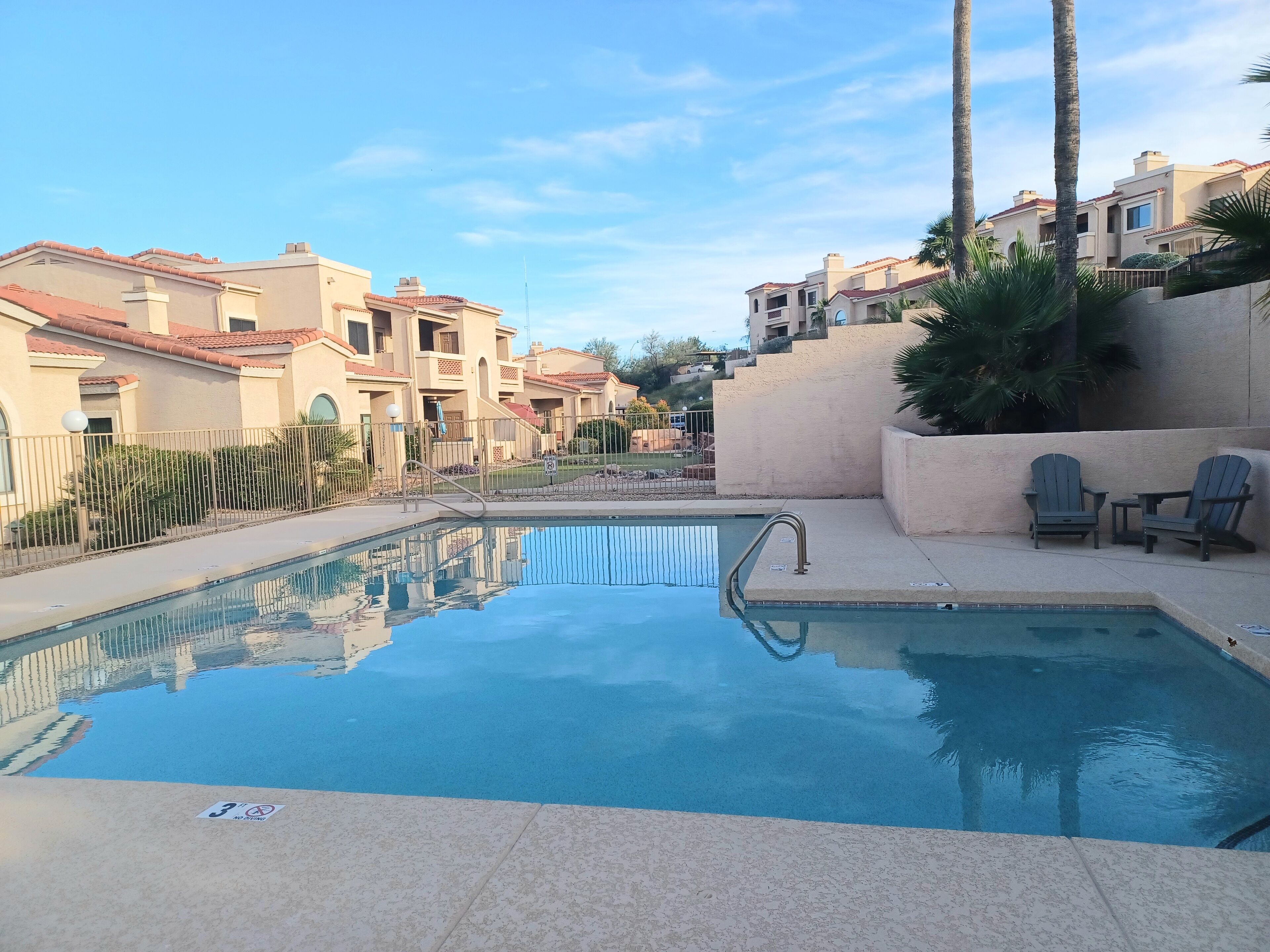 Une piscine avec un panneau indiquant qu’il est interdit de plonger, entourée d’immeubles d’habitation et de palmiers.