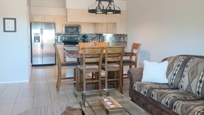 A modern living room with a glass coffee table, a patterned sofa, and a dining area with wooden chairs and a kitchen in the background. - Sparkling Clean 'Javelina Hideaway' in Beautiful Fountain Hills (Fountain Hills)