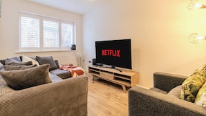 Una sala de estar con una televisión de pantalla plana mostrando 'NETFLIX', un sofá, una mesa de centro y una lámpara.