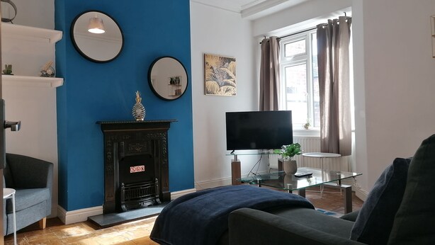 A living room with a blue accent wall, a fireplace, a flat-screen TV, and a glass coffee table. - Ermine Road -  a house that sleeps 7 guests  in 4 bedrooms (Chester)