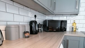 A modern kitchen with grey cabinets, a microwave, a coffee maker, and a bottle of olive oil on the counter. - Ermine Road -  a house that sleeps 7 guests  in 4 bedrooms (Chester)