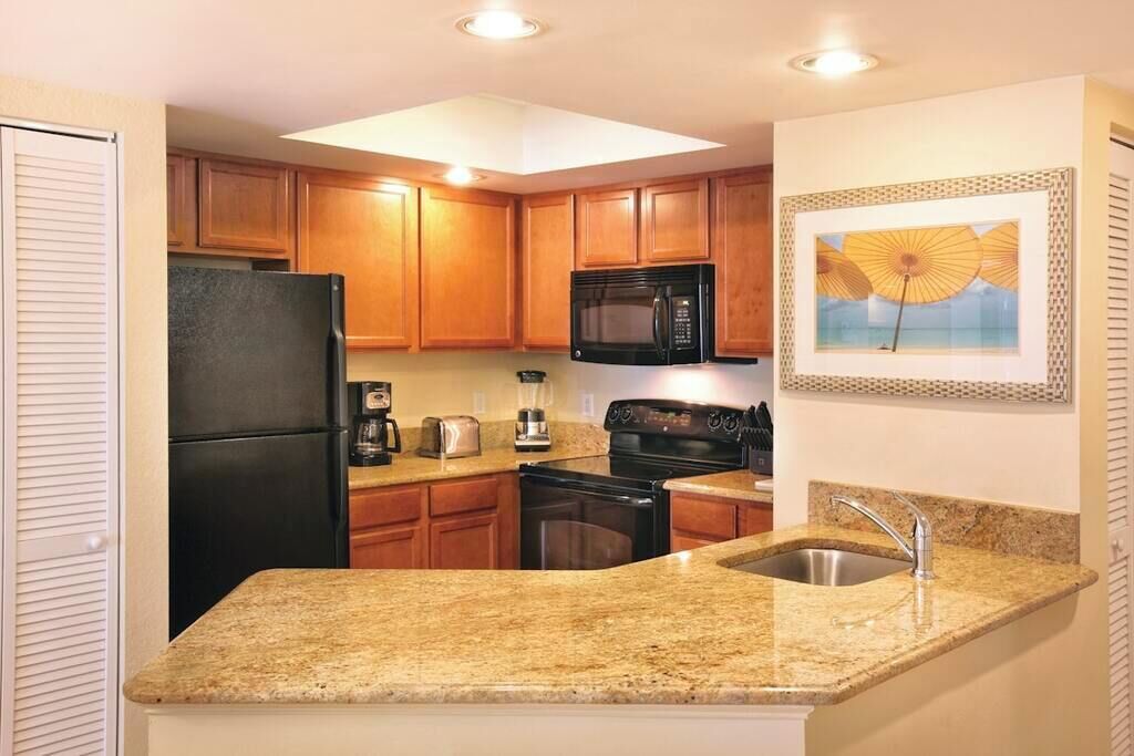 A compact kitchen with wooden cabinets, a black refrigerator, a microwave, a stove, and a sink.