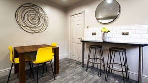 A kitchen with a wooden table and yellow chairs, a white door, and a mirror above the counter. - Brattan Road -  a house that sleeps 5 guests  in 5 bedrooms (Oxton)