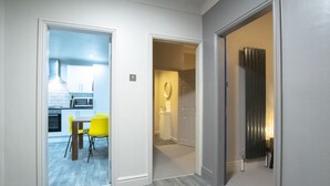 A hallway with a dining area featuring a table and chairs, a kitchen visible through an open door, and a bathroom with a towel rack. - Brattan Road -  a house that sleeps 5 guests  in 5 bedrooms (Oxton)