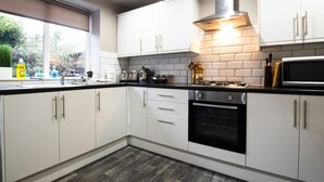 A modern kitchen with white cabinets, a black stove, and a window providing a view of greenery outside. - Brattan Road -  a house that sleeps 5 guests  in 5 bedrooms (Oxton)