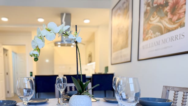 Un tavolo da pranzo con quattro bicchieri da vino, un vaso con orchidee bianche e una ciotola blu.