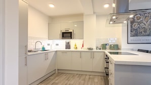 Cucina moderna con mobili bianchi, forno a microonde, lavello e piano di lavoro con diversi elettrodomestici e utensili.