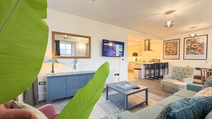 Un salon moderne avec un canapé, une table basse et un téléviseur. Il y a également un coin cuisine avec un bar et des chaises.
