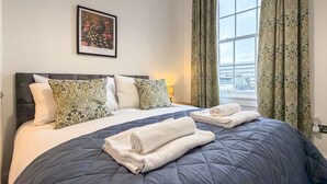Una camera d'albergo con un letto grande, cuscini decorati, un quadro incorniciato e vista sulla città attraverso una finestra.