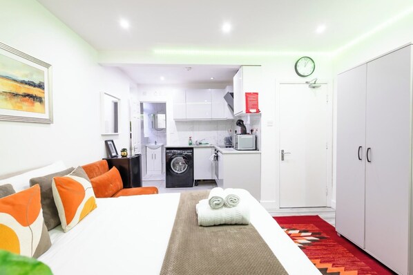 Una habitación de hotel con cama, sofá, lavadora, microondas y armario.