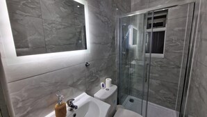 Ein modernes Badezimmer mit einer gläsernen Duschkabine, einem Waschbecken mit Handtuchspender und einer Toilette.